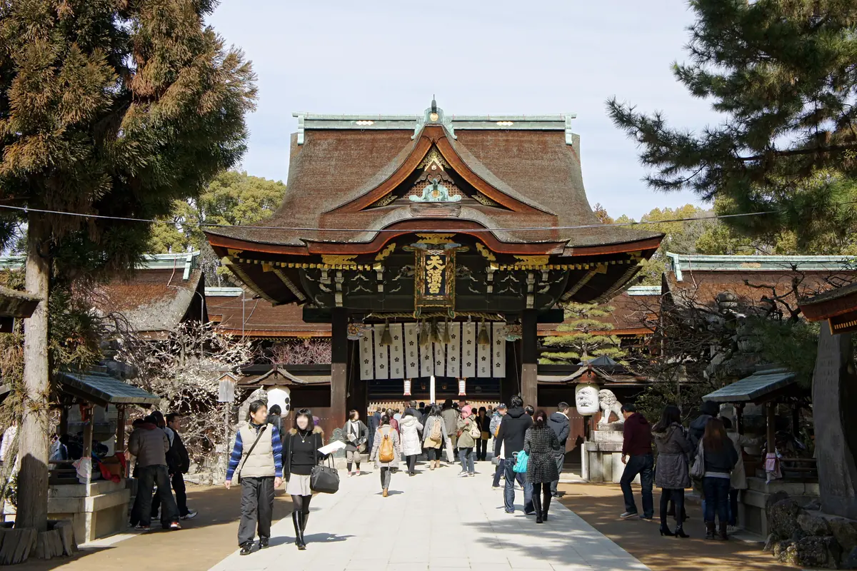 The main gate of Kitano Tenmangū in Kyoto, with plum trees in blossom and visitors walking up the approach